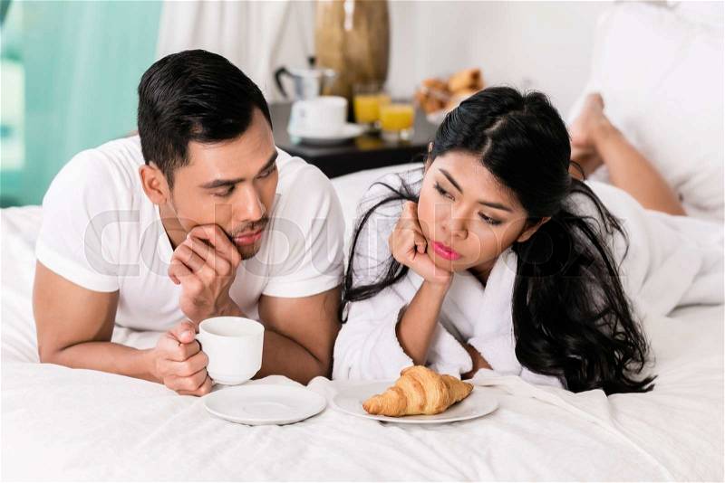 Marital issues - asian man feeling rejected by his wife, they are laying in bed, stock photo