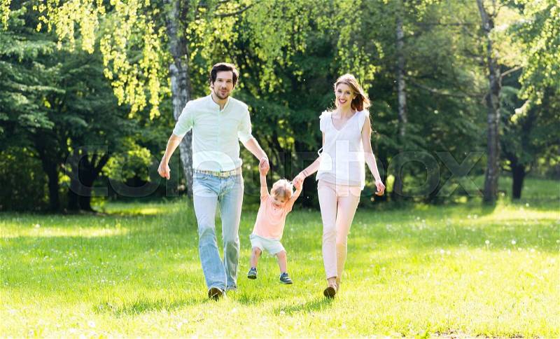 Family having walk together in summer holding hands and letting the little boy fly, stock photo