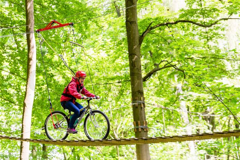Girl on bicycle on platform in high rope park, stock photo