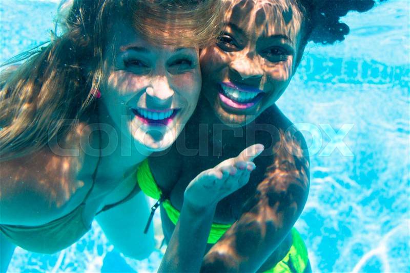Friends diving underwater in swimming pool, black and white girl, stock photo