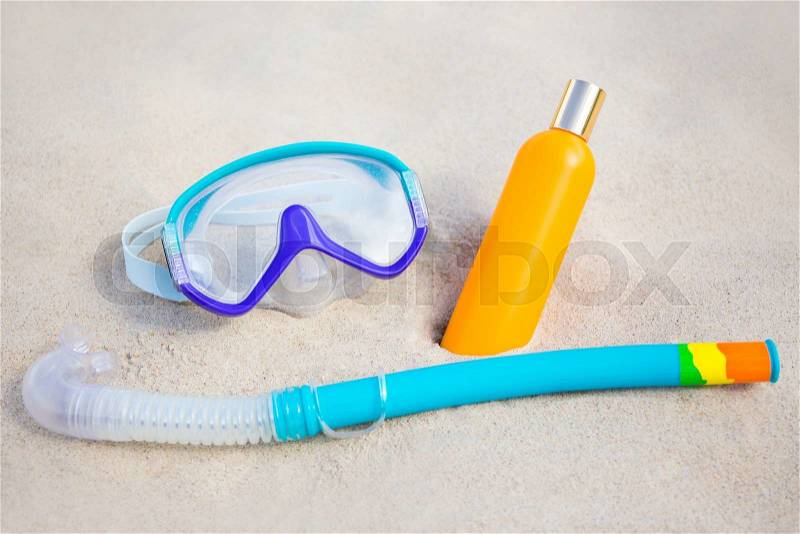 Summer concept - close up of diving mask and suntan lotion bottle on sandy beach, stock photo