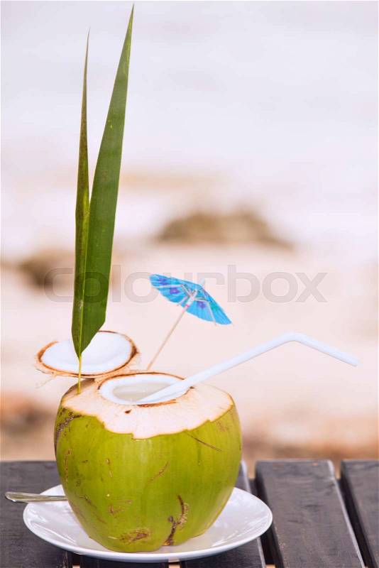 Coconut water drink served in coconut with drinking straw on the beach, stock photo
