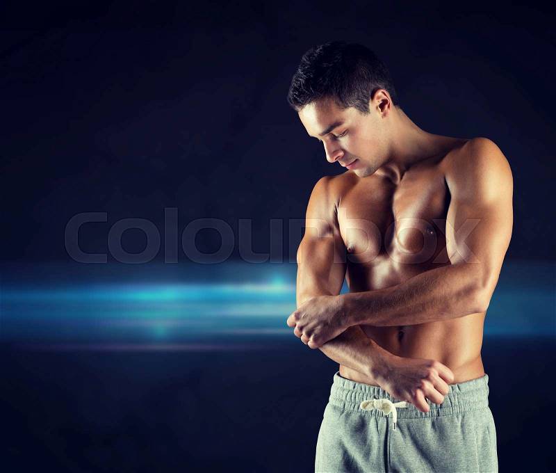 Pain, sport, bodybuilding, health and people concept - young male bodybuilder touching injured elbow over dark background, stock photo