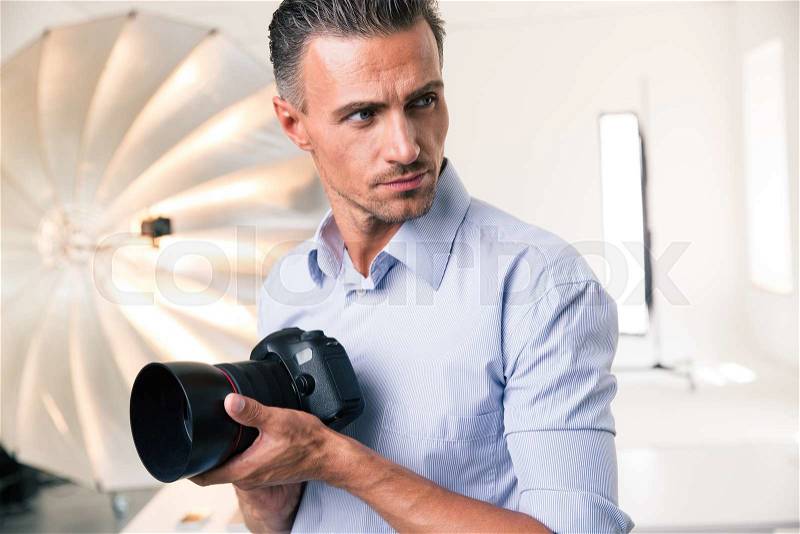 Portrait of a confident photographer holding camera and looking away in studio, stock photo