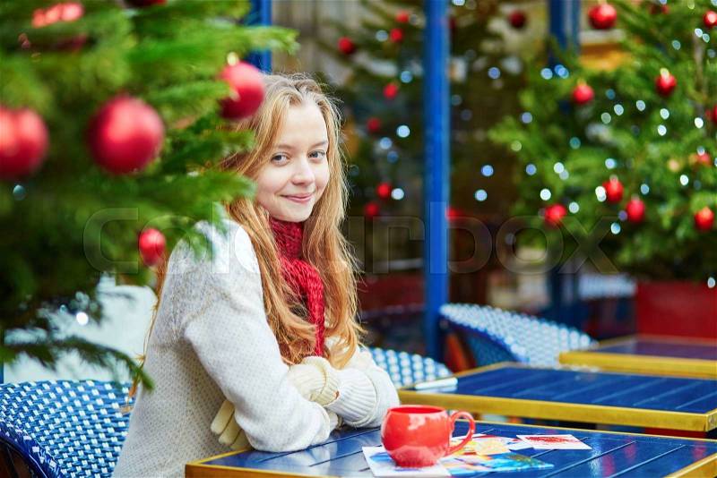 Girl drinking coffee and writing Christmas postcards in an outdoor Parisian cafe, stock photo