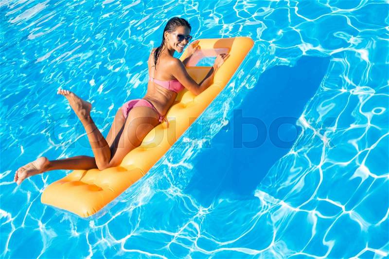 Portrait of attractive woman lying on air mattress in the swimming pool , stock photo