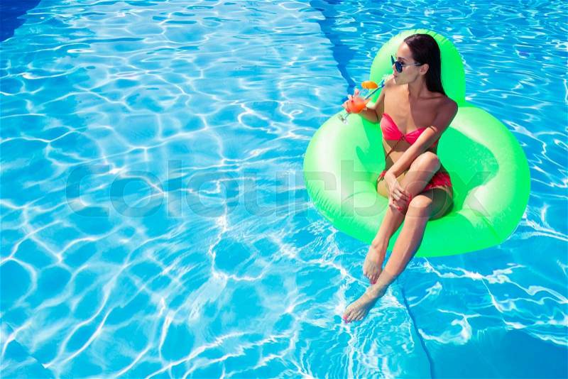 Portrait of a woman drinking cocktail on air mattress in swimming pool, stock photo