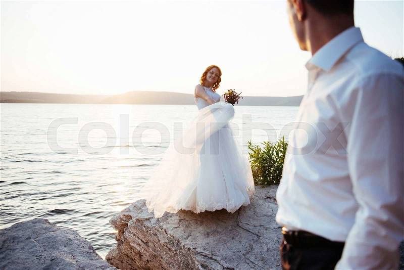 Beautiful lovely blonde bride and groom classy on the rocks, amid the sea at sunset, stock photo