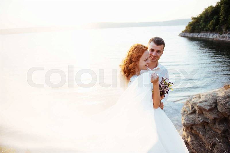 Beautiful lovely blonde bride and groom classy on the rocks, amid the sea at sunset, stock photo
