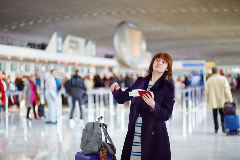 Beautiful young female passenger at check-in counter in the airport, holding her passport and boarding pass, stock photo