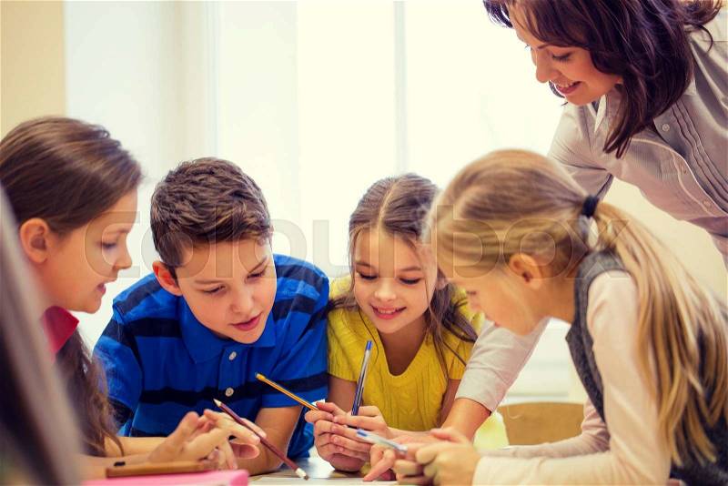 Education, elementary school, learning and people concept - teacher helping school kids writing test in classroom, stock photo