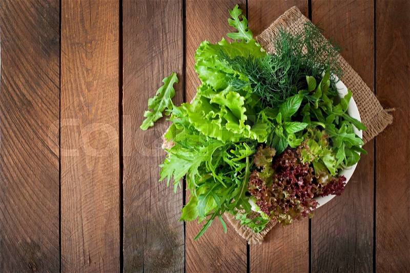Variety fresh organic herbs (lettuce, arugula, dill, mint, red lettuce) on wooden background in rustic style, stock photo