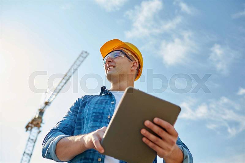 Business, building, industry, technology and people concept - smiling builder in hardhat with tablet pc computer over group of builders at construction site, stock photo