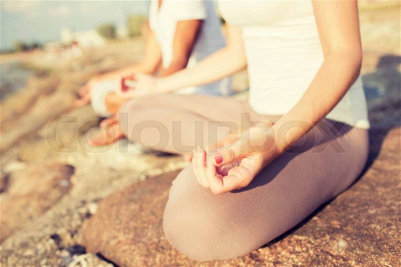Fitness, sport, people and lifestyle concept - close up of couple making yoga exercises sitting on pier outdoors, stock photo