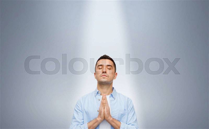 Faith in god, religion and people concept - happy man with closed eyes praying under ray of ligh over gray background, stock photo