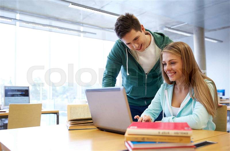 People, education, technology and school concept - happy students with laptop computer networking in library, stock photo