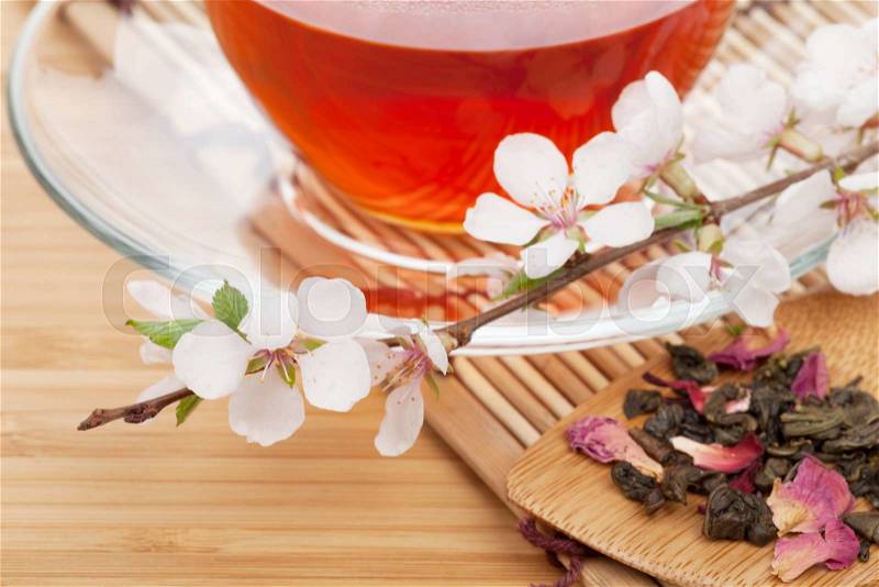 Japanese green tea and sakura branch over mat and bamboo table, stock photo