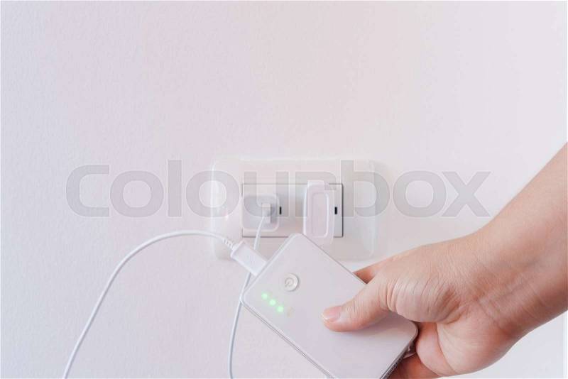 Female hand plugging in the wall electtric plug of her power bank in a socket, stock photo