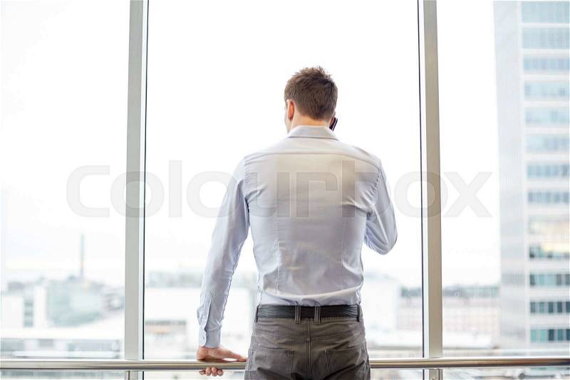 Business, technology and people concept - businessman calling on smartphone and looking out office window, stock photo
