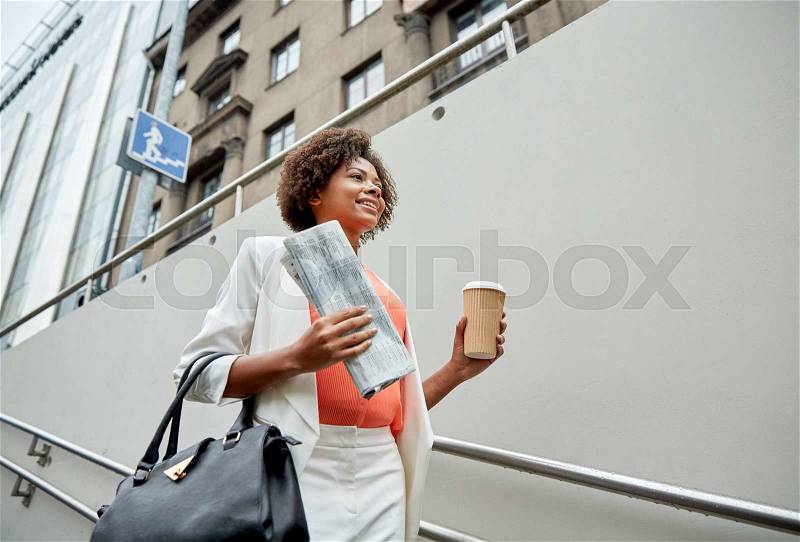 Business and people concept - young smiling african american businesswoman with coffee cup going down stairs into city underpass, stock photo