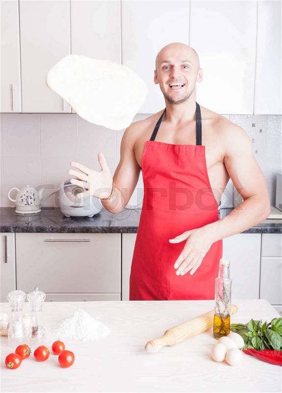 Muscle man cooking pizza in the kitchen, stock photo