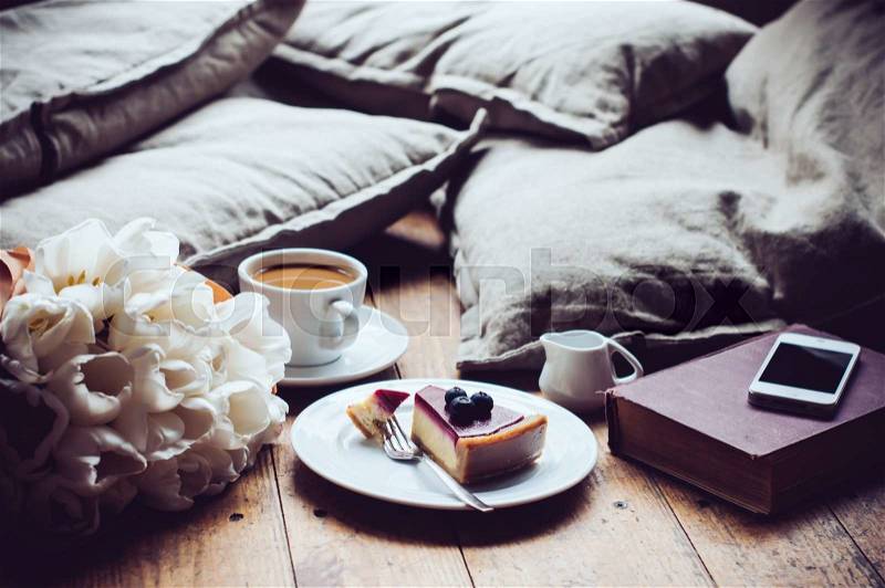 Pillows, a bouquet of tulips, coffee with milk, cheesecake and smartphone on a shabby wooden floor. Hipster lifestyle, stock photo