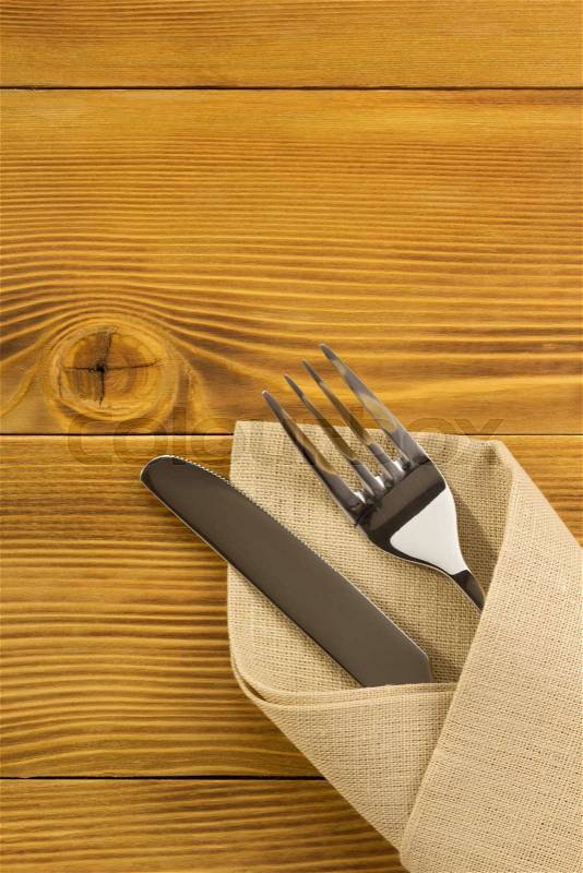 Knife and fork at napkin on wooden background, stock photo