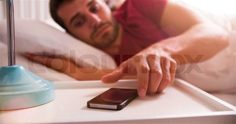 Man In Bed Woken By Alarm On Mobile Phone, stock photo