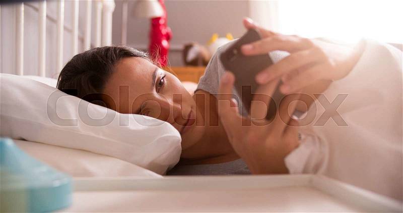 Woman Lying In Bed Checking Messages On Mobile Phone, stock photo