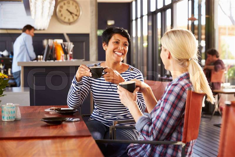 Two female friends talking at a coffee shop, stock photo
