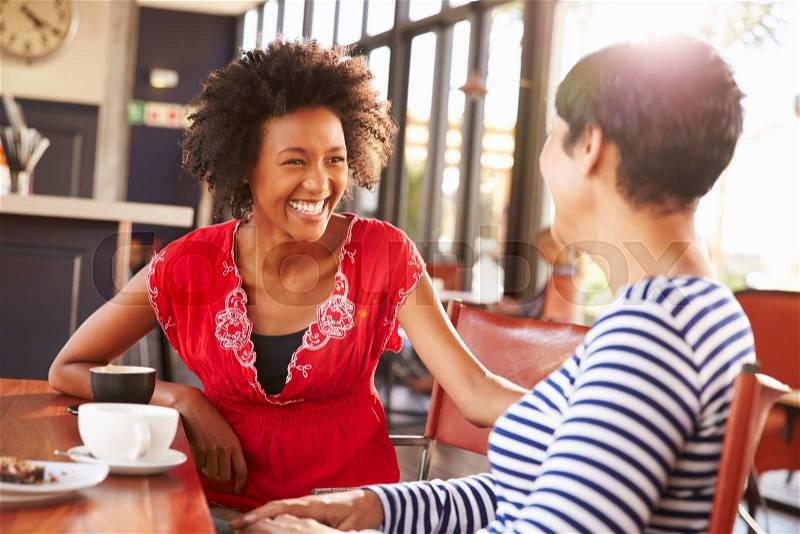 Two female friends talking at a coffee shop, stock photo