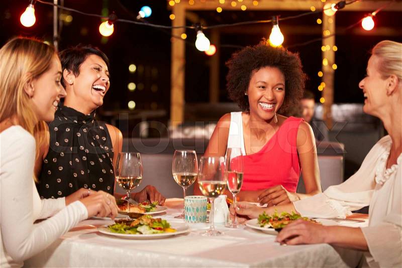 Group of female friends eating dinner at rooftop restaurant, stock photo