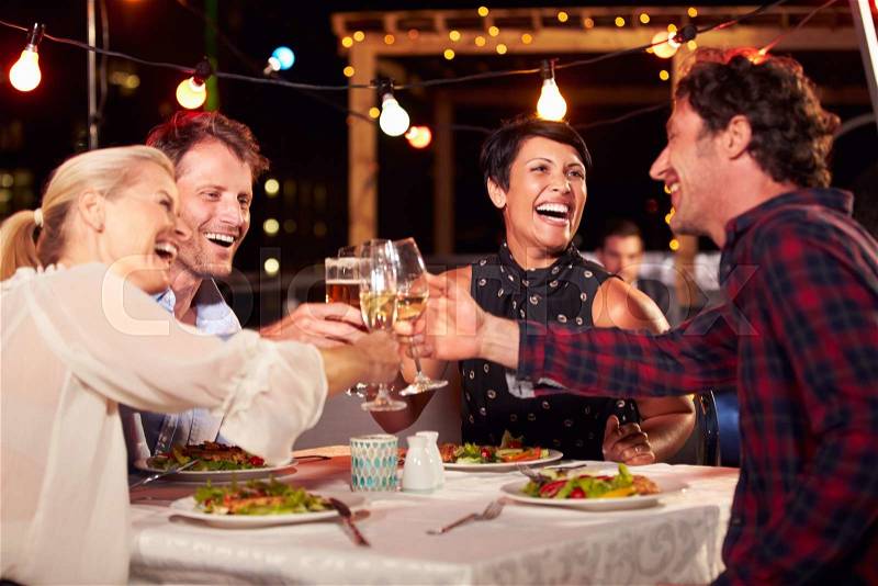 Group of friends eating dinner at rooftop restaurant, stock photo