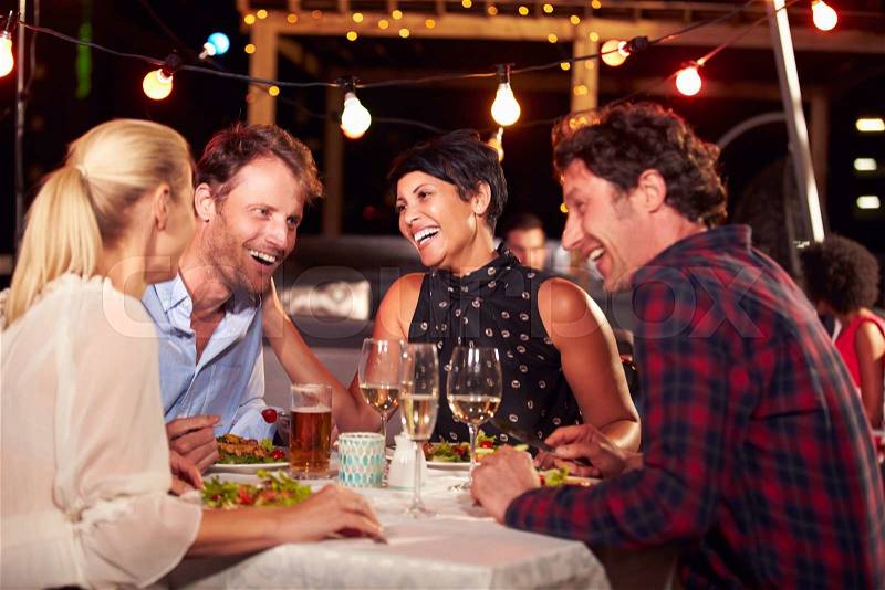 Group of friends eating dinner at rooftop restaurant, stock photo