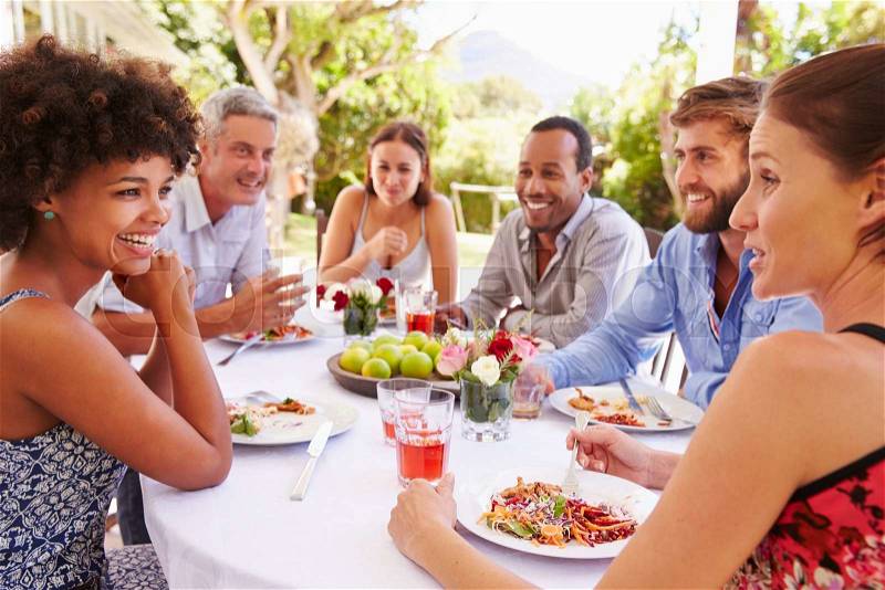 Friends dining together at a table in a garden, stock photo