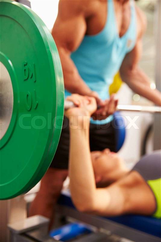 Woman lifting weights with trainer, focus on barbells, stock photo