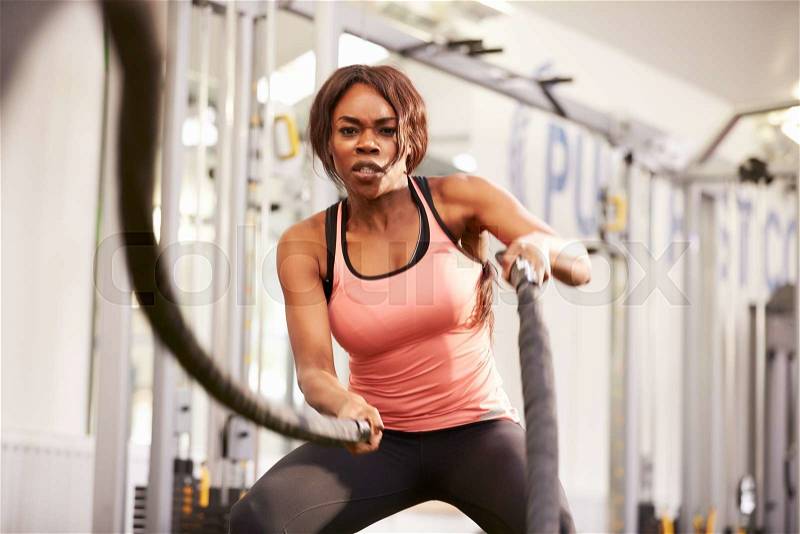 Young woman working out with battle ropes at a gym, stock photo