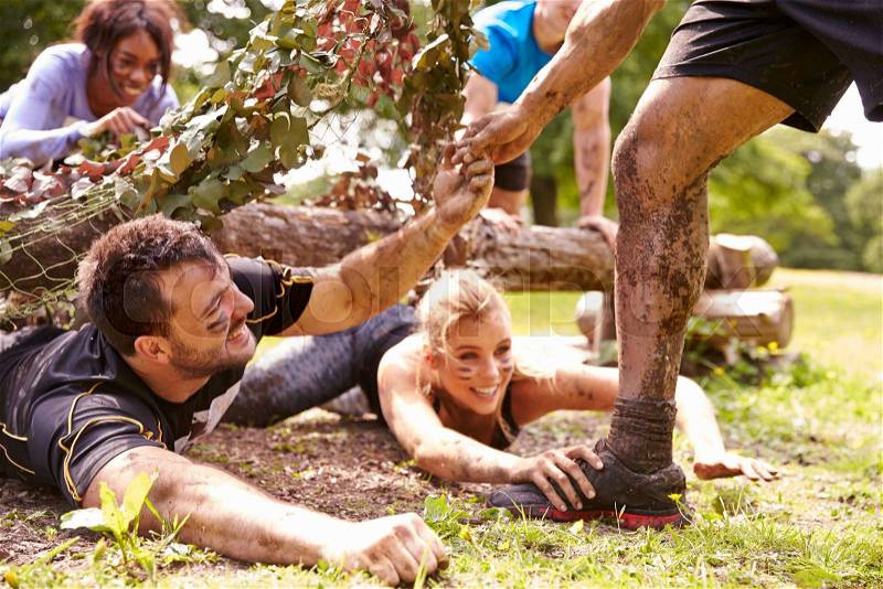 Assault course competitor helping others crawl under nets, stock photo