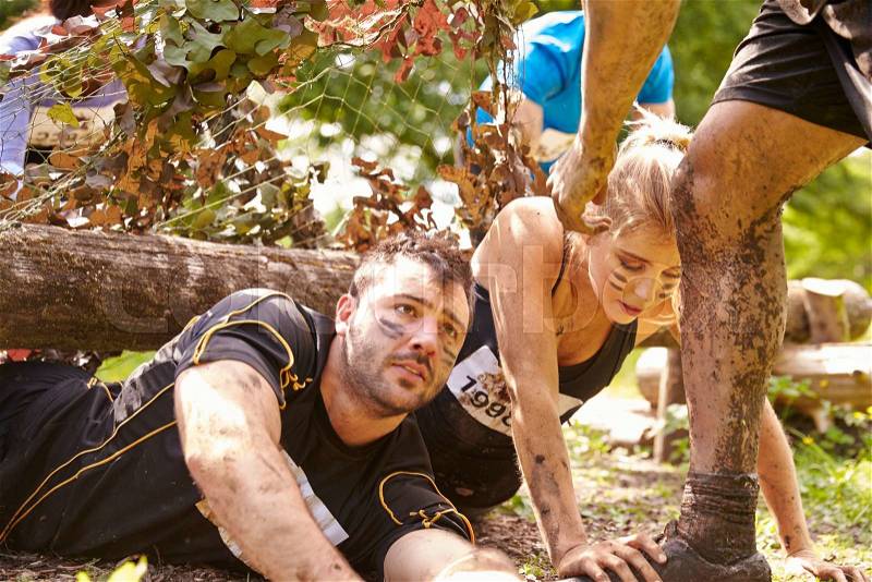 Assault course competitor helping others crawl under nets, stock photo