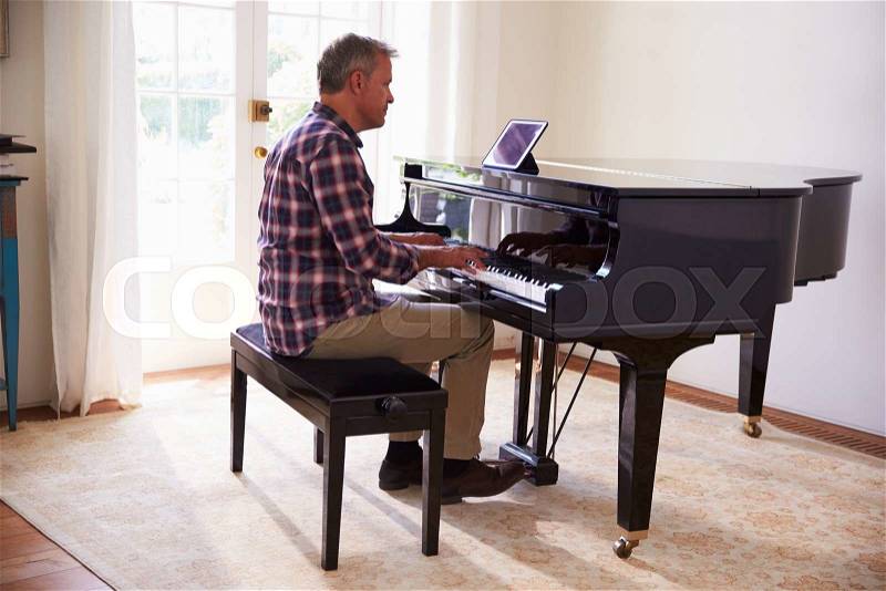 Man Learning To Play Piano Using Digital Tablet Application, stock photo