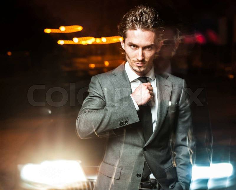 Handsome man in suit posing near car at night, stock photo