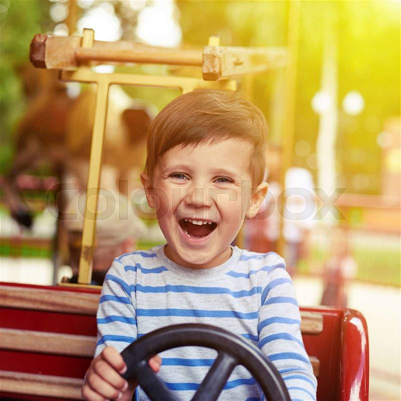 Happy little boy driving a car on merry-go-round, stock photo