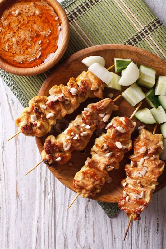 Chicken satay with a delicious peanut sauce and fresh salad on the plate closeup. vertical top view\, stock photo