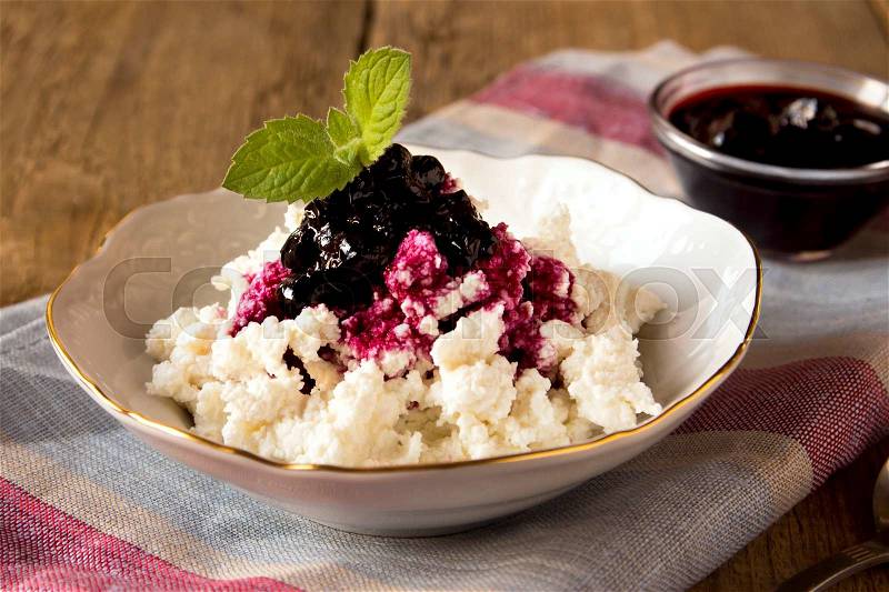 Cottage cheese with blueberry jam and mint for breakfast in a bowl over rustic wooden table, stock photo