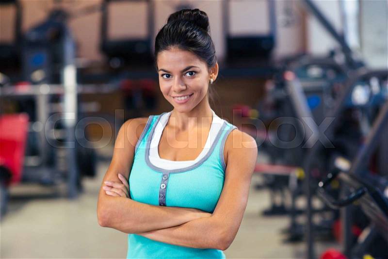 Portrait of a cheerful sports woman standing with arms folded in fitness gym, stock photo