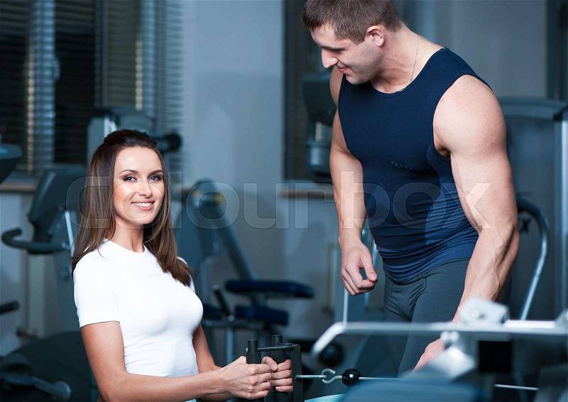Beautiful woman dressed white shirt, blue leggings and sneakers posing in gym with muscular personal trainer.Fashion look.Healthy life.Wellness.Lifestyle.Athletic body.Exercises.Healthcare, stock photo