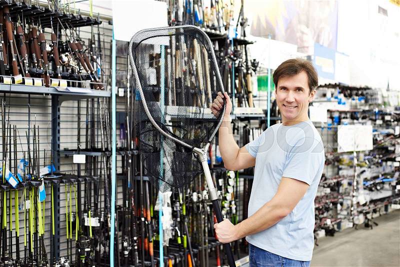 Man chooses landing net for fishing in the sports shop, stock photo