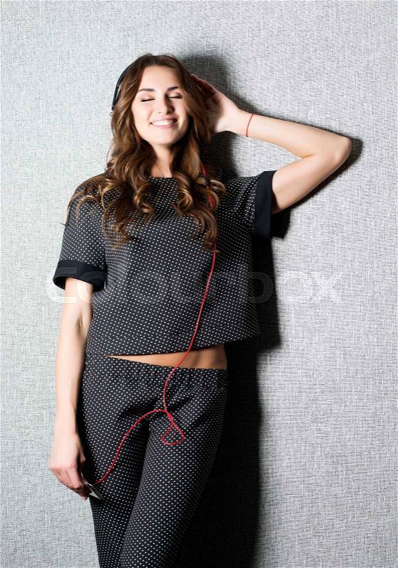 Beautiful smiling long haired DJ woman with black earphones in dark stylish suit poses on grey background.White teeth.Charming smile.Well-groomed skin.Fashion look.Glamorous clothes.Studio, stock photo