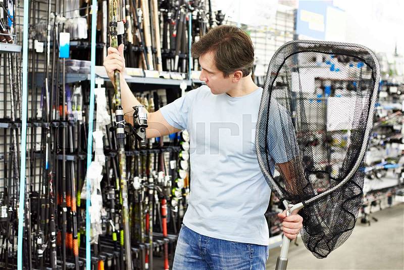 Man chooses fishing rod and landing net in the sports shop, stock photo