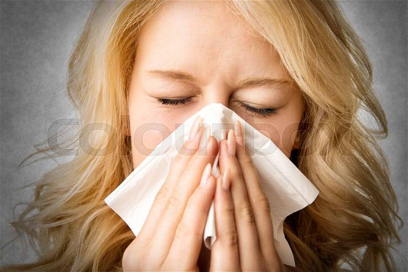 Portrait of a ill blond woman who is sneezing in a tissue, stock photo